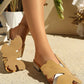 Woman's legs wearing tan Aevana bohemian flat slides, featuring oversized leaf embellishments and crystal-adorned low block heels, styled in an outdoor setting.