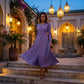 Amethyst Purple pleated V-neck midi dress with long sleeves, flowing on a woman descending steps in an illuminated evening setting.