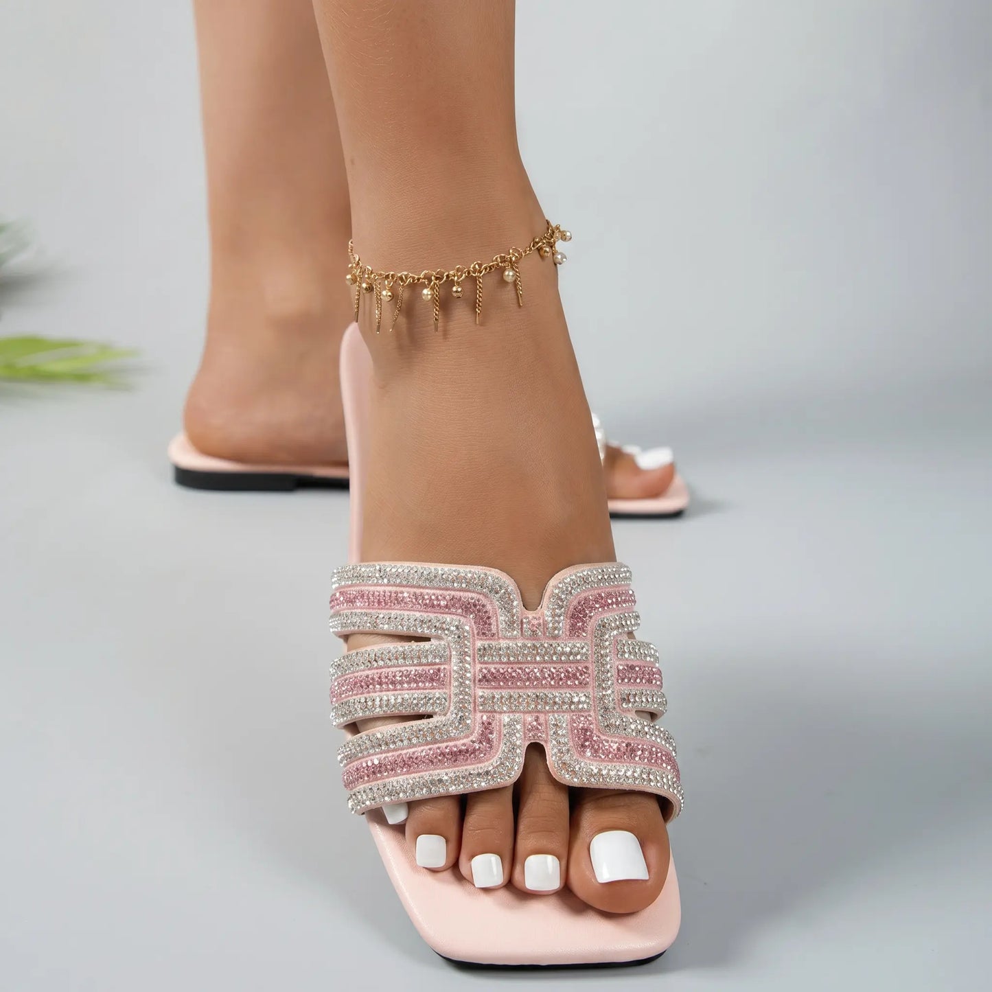 Close-up front view of Ayori pink rhinestone flat slide sandals, showcasing the embellished single band strap, square toe, and padded footbed on a foot with white toenails.