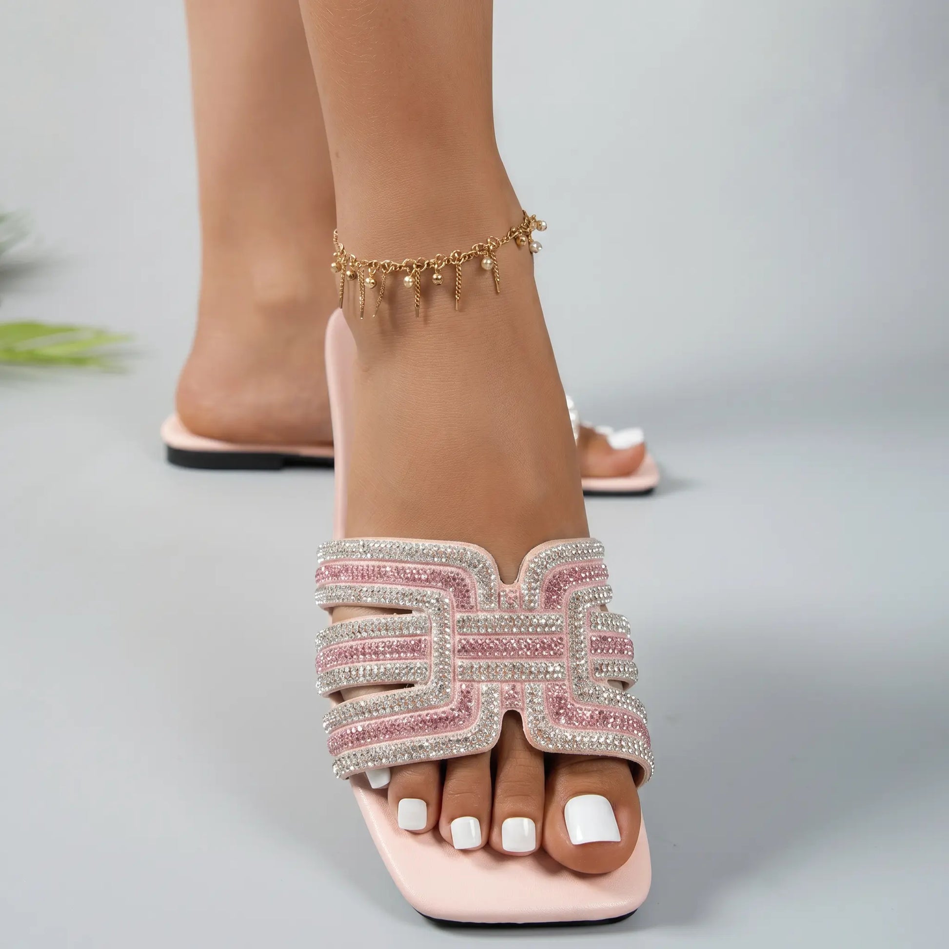 Close-up front view of Ayori pink rhinestone flat slide sandals, showcasing the embellished single band strap, square toe, and padded footbed on a foot with white toenails.