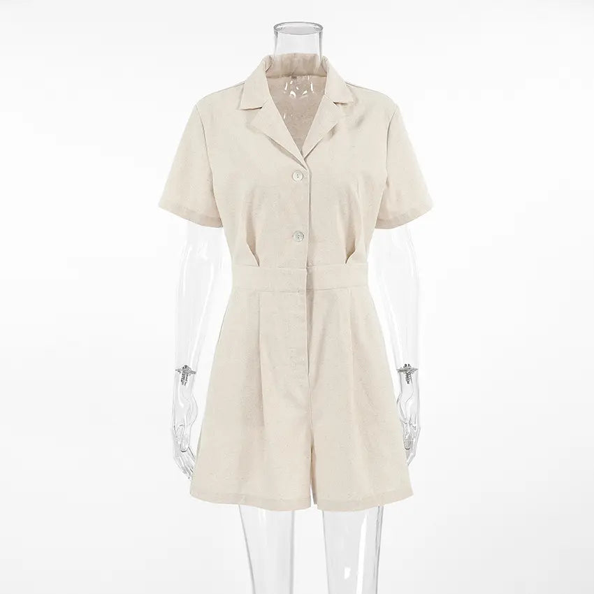 Azkari oat-beige linen-blend jumpsuit featuring a camp collar, short sleeves, button-down front, and wide-leg shorts, shown on a mannequin against a white studio background.