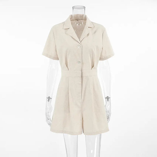 Azkari oat-beige linen-blend jumpsuit featuring a camp collar, short sleeves, button-down front, and wide-leg shorts, shown on a mannequin against a white studio background.