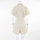 Azkari women's oat-beige linen-blend short-sleeved jumpsuit with wide-leg shorts, shown from the back view on a mannequin against a studio background. Features a camp collar and self-tie belt.