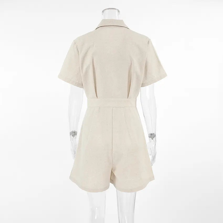Azkari women's oat-beige linen-blend short-sleeved jumpsuit with wide-leg shorts, shown from the back view on a mannequin against a studio background. Features a camp collar and self-tie belt.
