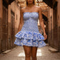 Woman in a blue and white strapless smocked mini dress with tiered ruffle skirt and eyelet embroidery, walking in a historic stone alleyway.