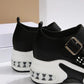 Close-up side view of black women's platform sneakers featuring a white sculpted sole with a visible translucent air cushion heel and a buckled strap.