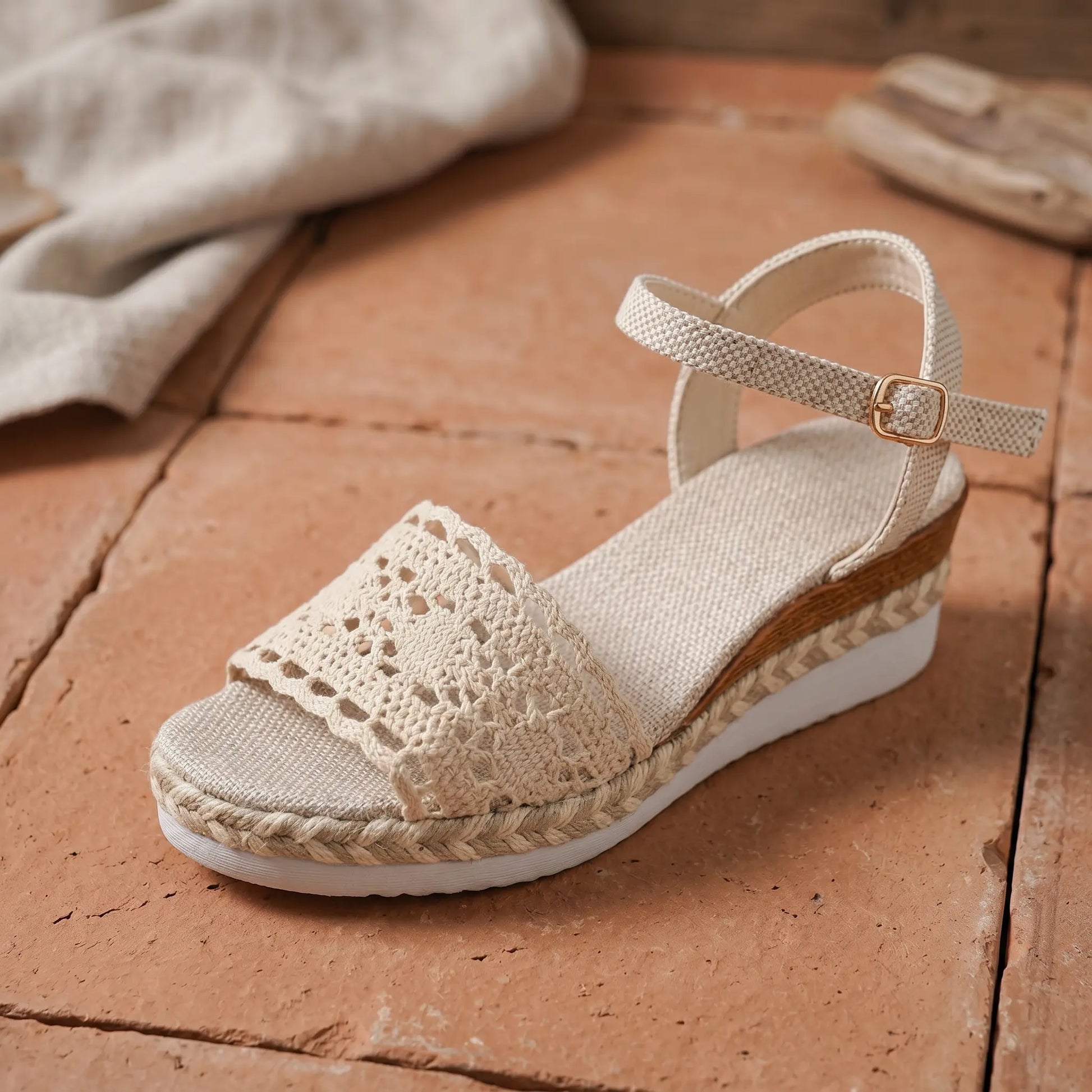 Side view of a warm beige espadrille wedge sandal featuring intricate crochet lace overlay on the vamp, jute-wrapped heel, and an antique gold-tone buckle on the ankle strap.