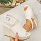 Beige espadrille wedge sandals worn on a foot, showcasing the peep-toe design, jute-wrapped wedge, and adjustable ankle strap, with another sandal held in hand. Features a textured suede-like upper and natural bohemian styling.