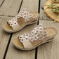 Beige bohemian wedge sandals for women featuring intricate laser-cut floral motifs on a single wide strap and a contoured wedge heel, displayed on a rustic wooden surface.