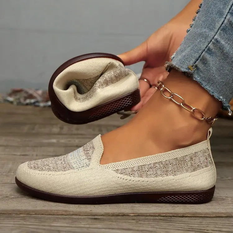 Warm beige breathable knit loafers featuring a geometric pattern and delicate crystal embellishment on the vamp, worn on a woman's foot with denim jeans and a gold ankle chain.