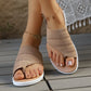 A close-up view of beige woven knit thong sandals worn on a model's feet, showcasing the intricate geometric pattern and contoured footbed on a wooden deck.