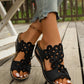 Woman's feet wearing black Zylphra bohemian wedge sandals with intricate floral laser-cut detailing and a cushioned footbed, shown on a wooden deck.