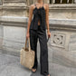 A woman models a black bohemian linen halter neck top with adjustable tie and matching wide-leg trousers in an urban outdoor setting, showcasing an elegant summer outfit.