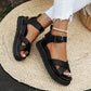 Black chunky platform sandals with criss-cross straps and buckle ankle closure, worn by a model with ripped white jeans on a woven mat.