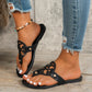 Black embellished flat thong sandals with ornate circular cut-out design and gold stud accents shown on a person's feet with ripped jeans.