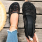 Black sheer mesh ballet flats adorned with delicate floral embroidery, faux pearls, and matte beads, shown on a foot with ripped jeans and a gold anklet, next to another shoe on a wooden surface.