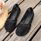 Black Lyraen embellished mesh ballet flats with intricate floral embroidery and pearl details, shown from a three-quarter angle on a weathered wooden surface with a straw hat.