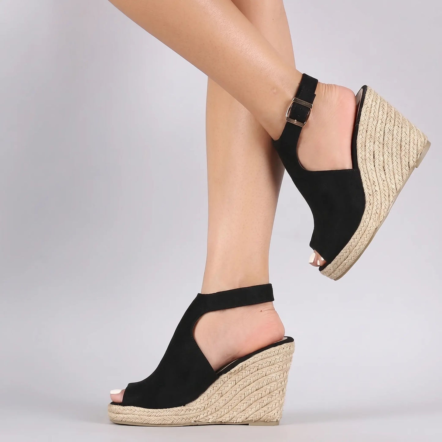 Black espadrille wedge sandals for women, featuring a peep-toe design, adjustable ankle strap with gold buckle, and a natural jute sole. Shown on a model's feet.