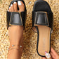Black Zovial flat slide sandals featuring a square gold buckle with a cream inlay, worn on a foot adorned with a jeweled anklet and pearl ring.