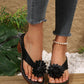 Women's black Kaelis floral platform sandals with chunky wood-effect heels shown on a model's feet with distressed denim jeans, styled on a natural wood and pebble background.
