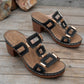 Black heeled platform slide sandals with geometric gold-tone hardware and white contrast stitching, shown from a three-quarter angle on a wooden surface.