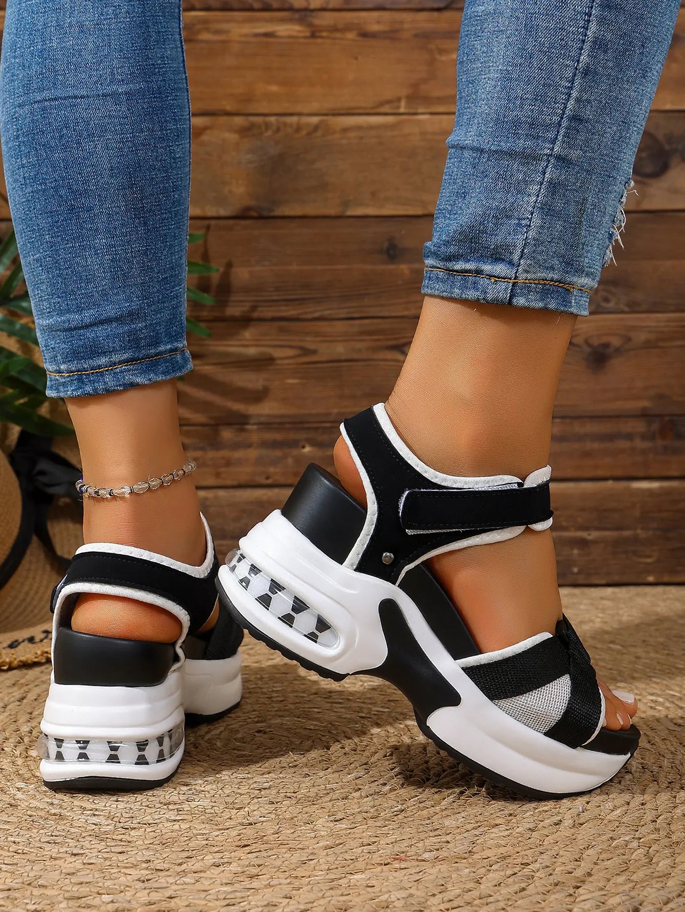 Women's black and grey woven textile platform sandals with a white stacked sole and transparent air cushion heel, shown on feet wearing blue jeans.