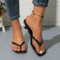 A pair of black heeled thong sandals with a square toe and sculptural block heel, worn by a model on a grey floor with a textured white background.