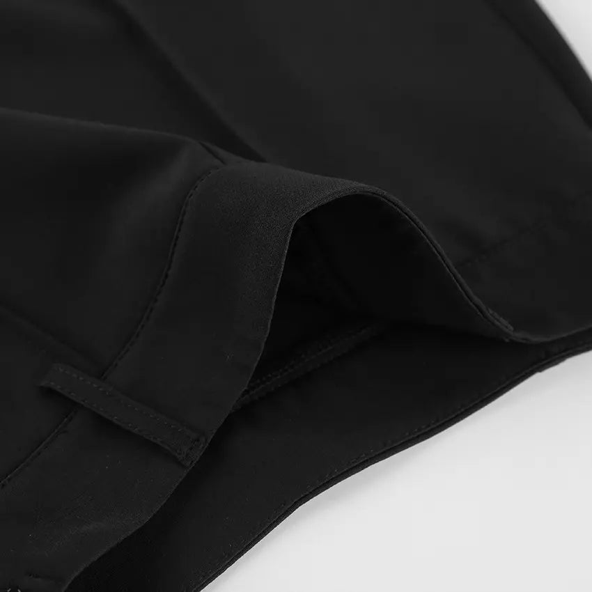 Close-up view of the waistband and front pleats of black high-waisted tailored shorts, showcasing the smooth matte fabric and precise tailoring details.