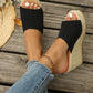Black knitted espadrille wedge sandals with open toe, worn by a woman on a wooden boardwalk, styled with blue denim jeans and a gold anklet.