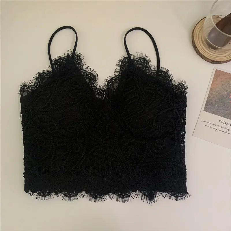 Black Zyrin lace cropped camisole with delicate floral crochet pattern, deep v-neck, and eyelash trim, laid flat on a light background with subtle props.