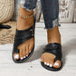 Black leather flat sandals with a toe-thong design and crisscross straps featuring an adjustable ankle buckle, styled with distressed denim.