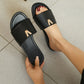 Black leather slide sandals with a polished gold-tone 'V' logo emblem, shown worn on a foot with manicured nails against a grey tiled floor.