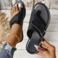Close-up top-down view of black leather toe-thong flat sandals with crisscross straps and white contrast stitching, shown on feet with a gold anklet and ripped jeans.