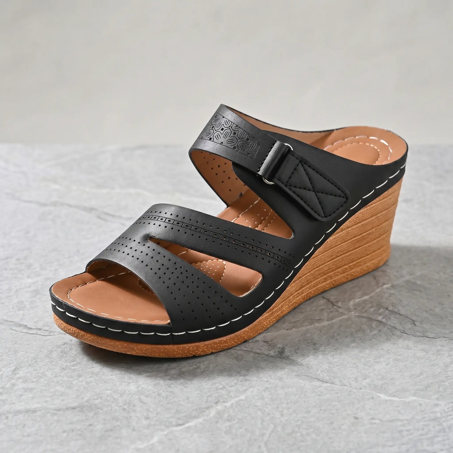 Black Zephira women's wedge sandal with peep-toe, laser-cut floral perforations, adjustable hook-and-loop strap, and white contrast stitching on a wood-grain wedge heel.