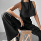 Woman wearing a black sleeveless crop top and high-waisted wide-leg trousers made of a linen blend, styled for effortless chic. The model is seated, showcasing the set's silhouette and texture.