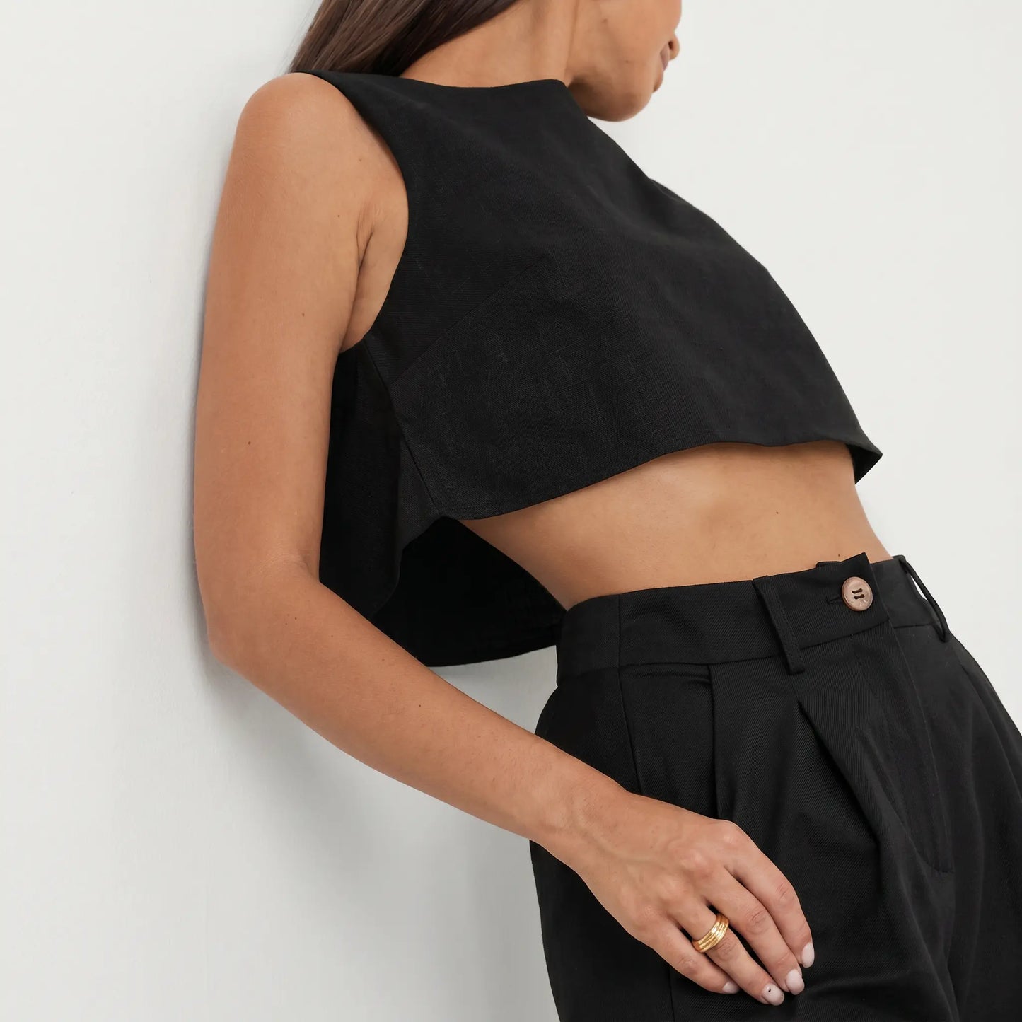 A black linen blend cropped sleeveless top and high-waisted wide-leg trousers, shown from a three-quarter view on a model. The set features a matte, slubbed texture and a minimalist design.