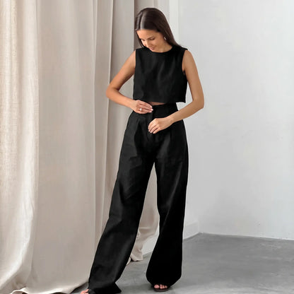 A woman wears a black linen blend crop top and high-waisted wide-leg trousers set, styled for effortless summer chic. The sleeveless top and flowing pants feature a natural, textured matte finish.