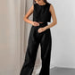 A woman wears a black linen blend crop top and high-waisted wide-leg trousers set, styled for effortless summer chic. The sleeveless top and flowing pants feature a natural, textured matte finish.