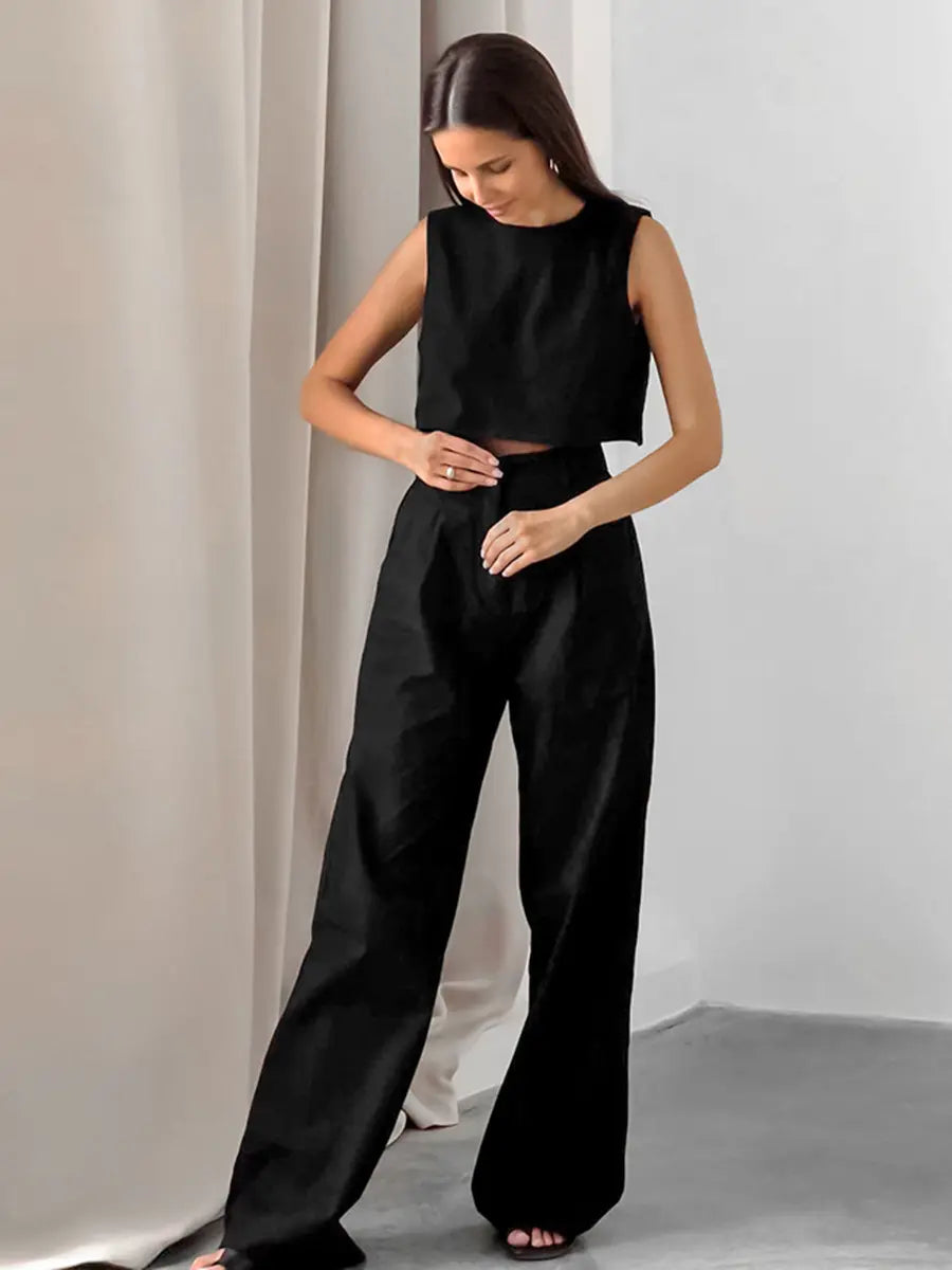 A woman wears a black linen blend crop top and high-waisted wide-leg trousers set, styled for effortless summer chic. The sleeveless top and flowing pants feature a natural, textured matte finish.