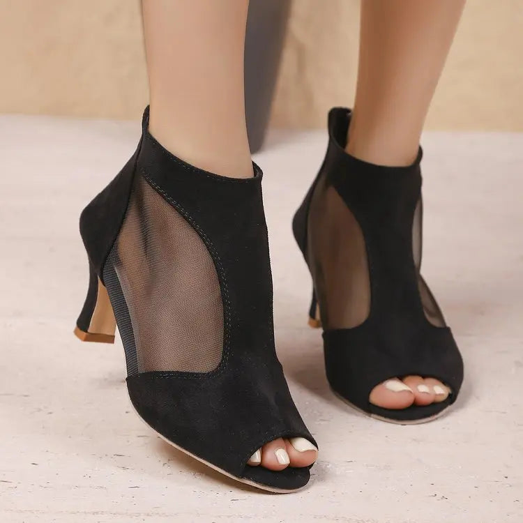 Elegant black suede-like peep-toe ankle boots with sheer mesh side panels and a slender stiletto heel, shown on a person's feet.