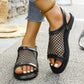 Black mesh sandals with faux leather accents and a silver buckle closure, shown worn on feet with white toenail polish, paired with denim jeans and a beaded anklet.