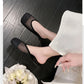 A pair of women's black diamond mesh mules with a square toe, elegantly worn by a model on a dark wooden floor with a bouquet of white flowers. The shoes feature a slip-on design and are paired with white fabric.
