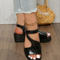 Black metallic embossed peep-toe wedge sandals with T-strap and ankle strap, worn by a model with distressed denim jeans and a gold anklet, styled with a woven bag.