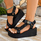 Black platform sandals with metallic gold and crinkled orange straps, featuring a lion's head detail and a royal blue elasticated heel strap, worn on feet with white toenails.