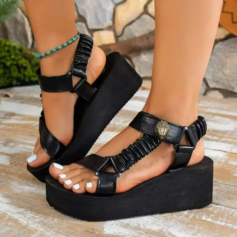 Black platform sandals with metallic gold and crinkled orange straps, featuring a lion's head detail and a royal blue elasticated heel strap, worn on feet with white toenails.