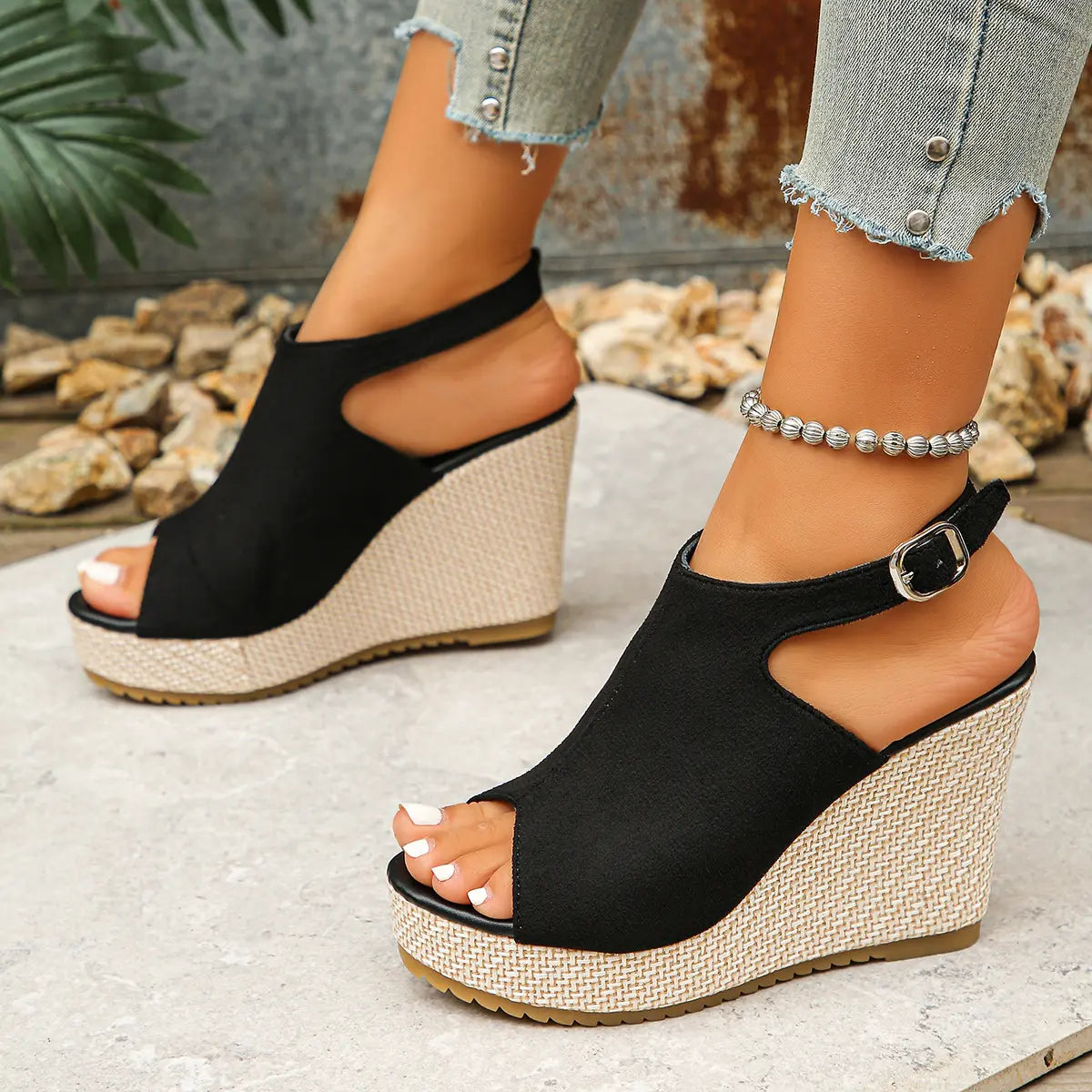 Black peep-toe espadrille wedge sandals worn by a model, featuring a jute-wrapped wedge, platform, and an adjustable ankle strap with buckle.