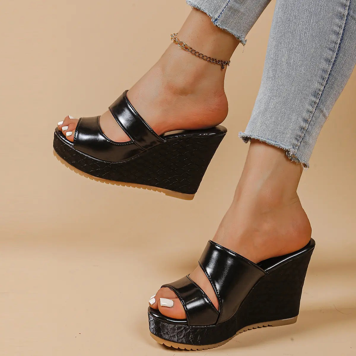 Black peep-toe platform wedge sandals with textured snake-effect heel and crossed straps, shown on a woman's foot with light blue jeans.