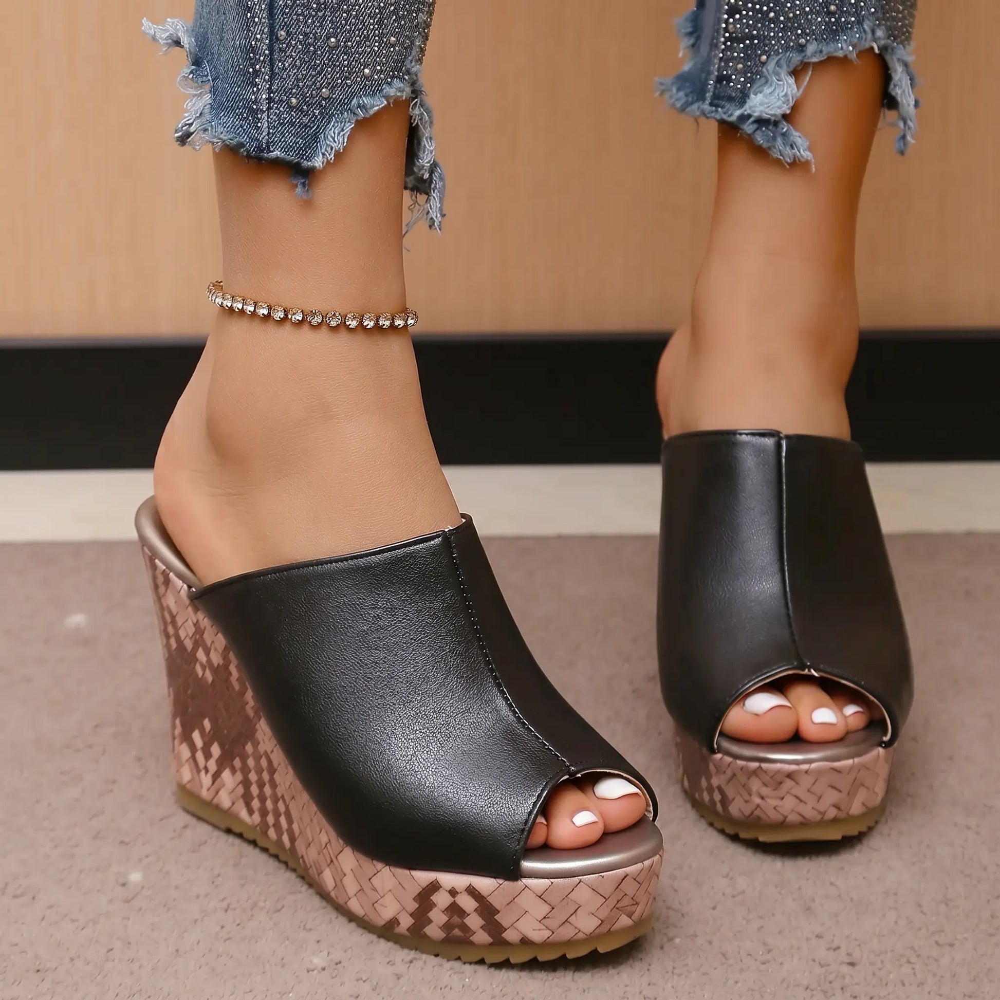 Black peep-toe wedge mule sandals worn by a person, showcasing the textured rose gold wedge and smooth polyurethane upper with distressed denim.