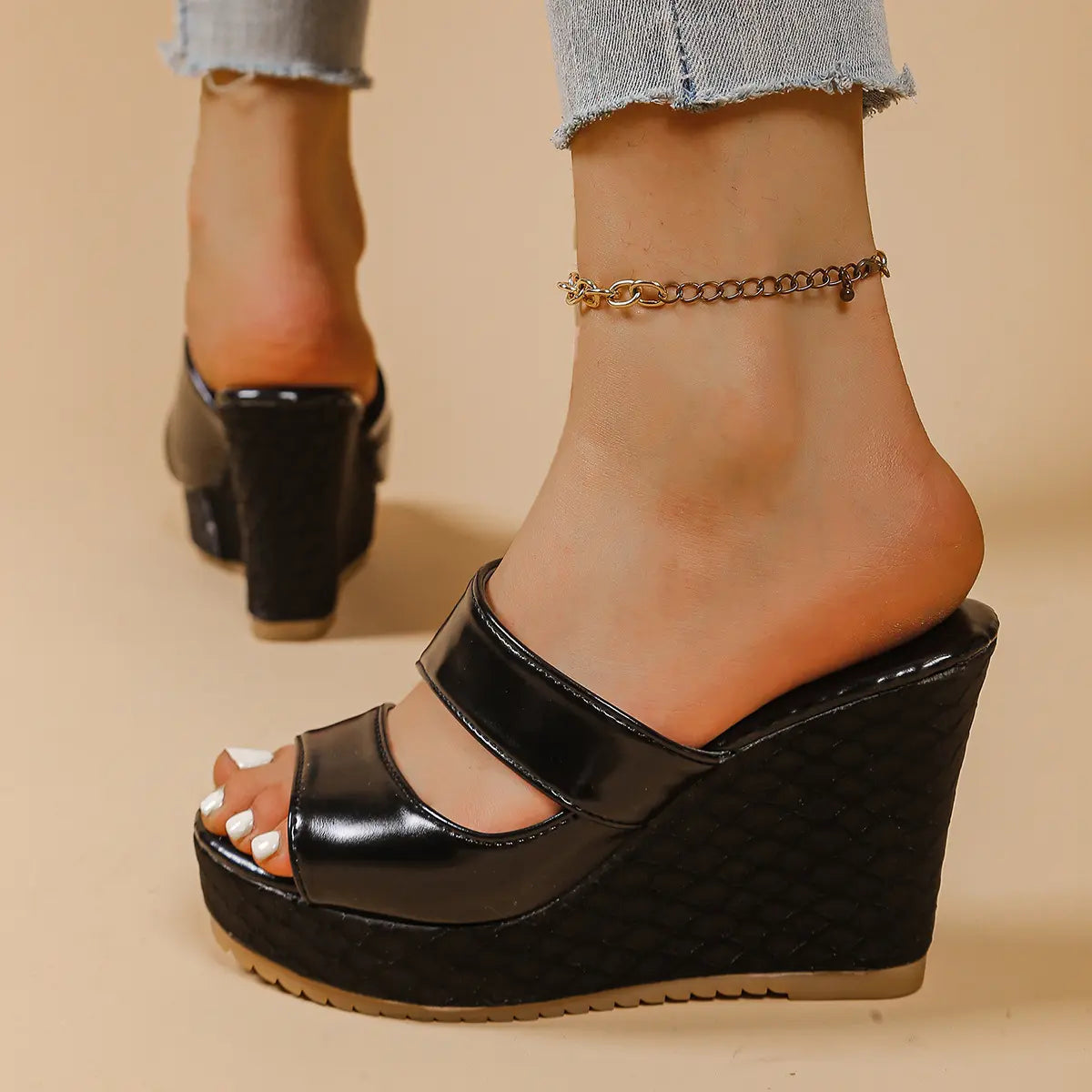 Black peep-toe platform wedge sandals with intersecting glossy straps and a textured snake-effect heel and platform, shown on a foot with a gold anklet.