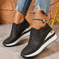 Women's black perforated wedge loafers with a subtle gold heel accent, styled with ripped blue jeans and a turquoise anklet. Features heart-shaped cutouts for breathability and comfort.